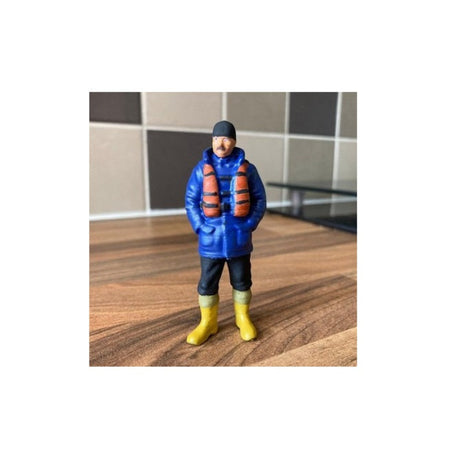 Figurine of a person wearing a blue jacket, orange life vest, and yellow boots 